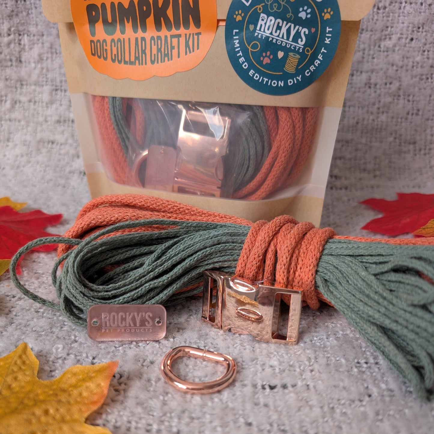 Pumpkin dog collar craft kit with ropes and hardware on a textured surface with autumn leaves.
