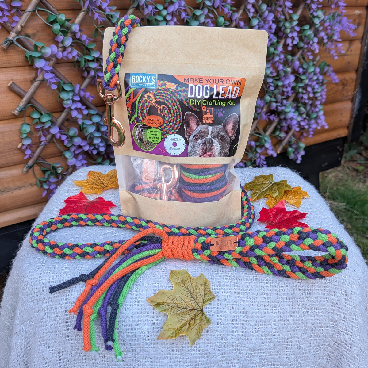 A dog leash set displayed outdoors on a white fabric-covered table. The set includes a tan paper bag package labeled 'DOGS LEASH' with a colorful braided leash and matching rope laid out in front.